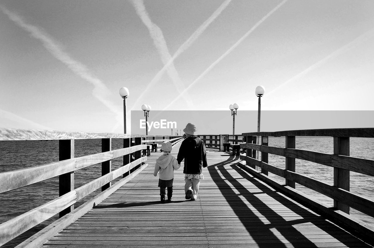 Rear view full length of girl walking with sister amidst sea on pier