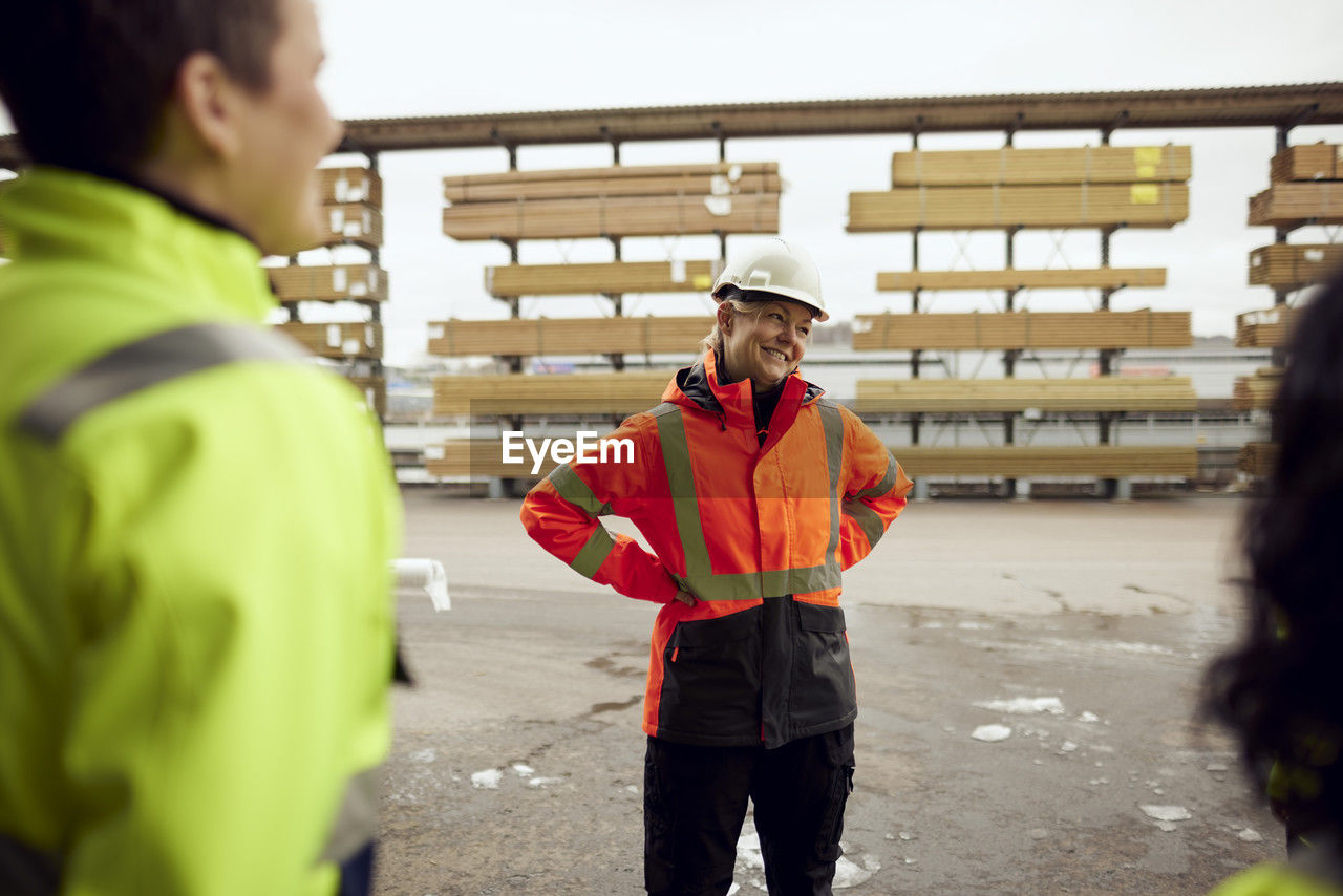 Smiling female worker in reflective clothing standing with colleagues at factory