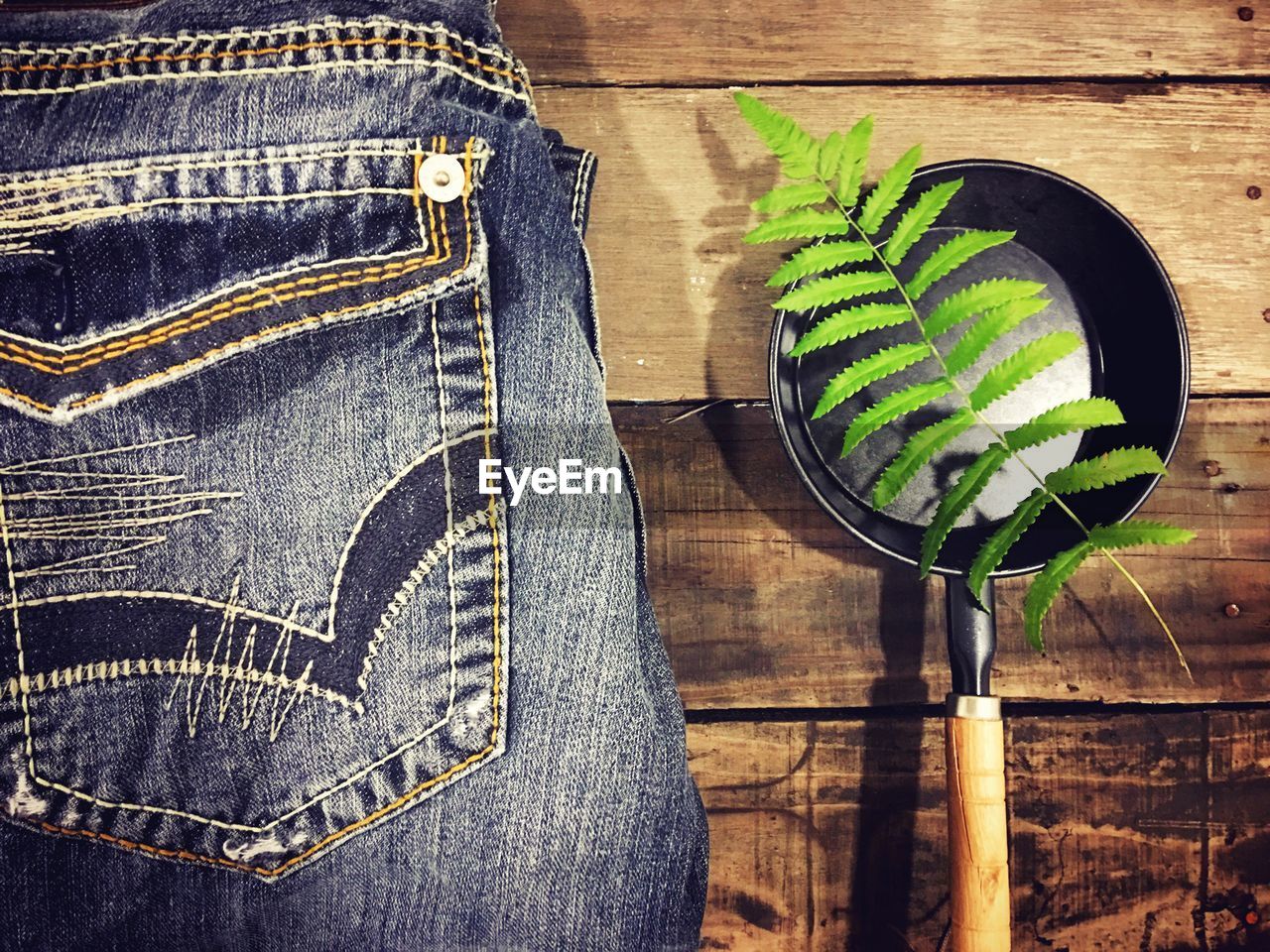 Fern in cooking utensil by jeans pant on wooden table