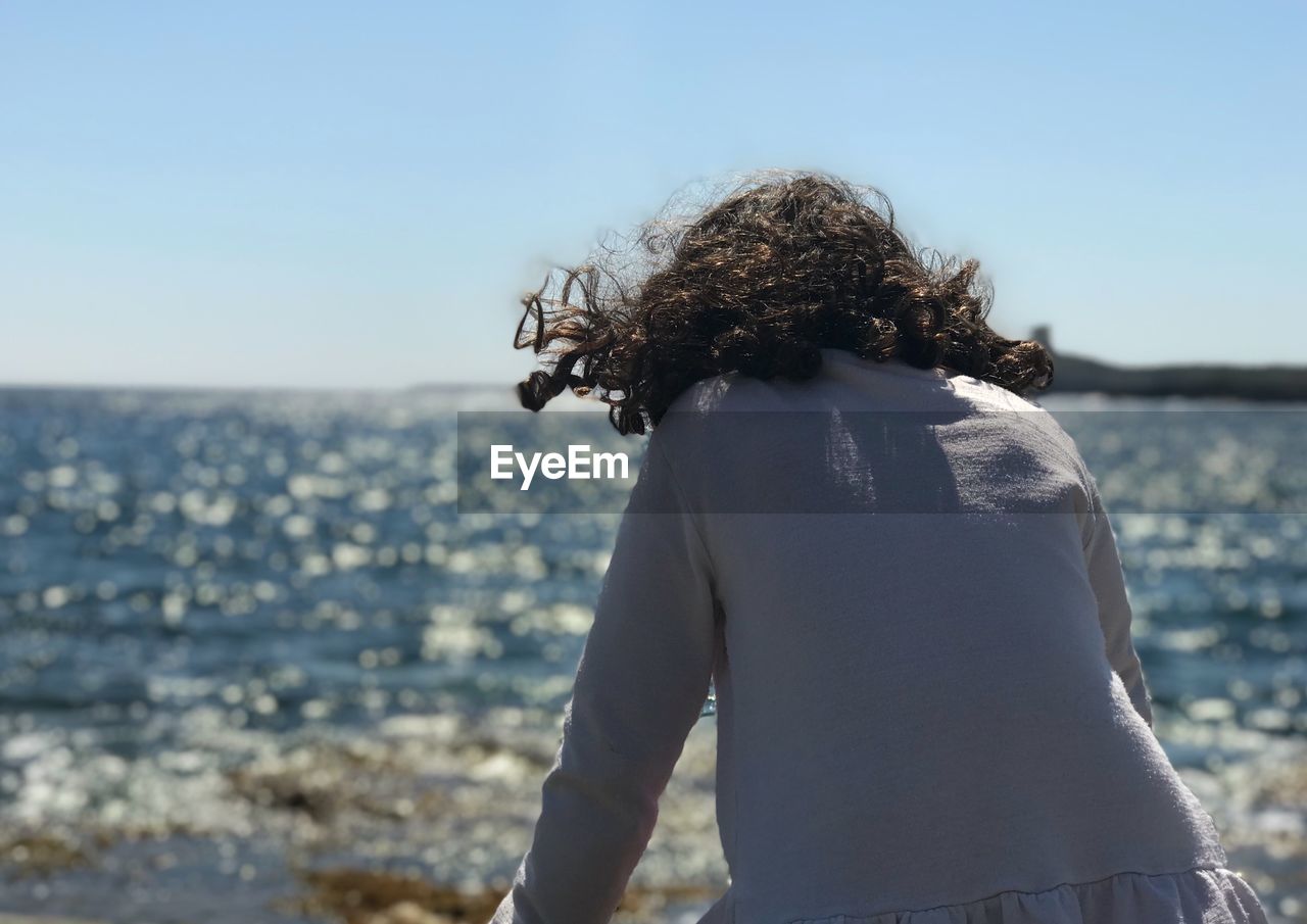 Rear view of woman sitting while looking at sea