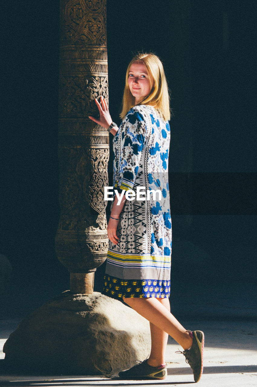 The blond girl standing near the old ancient  column. touch eternity