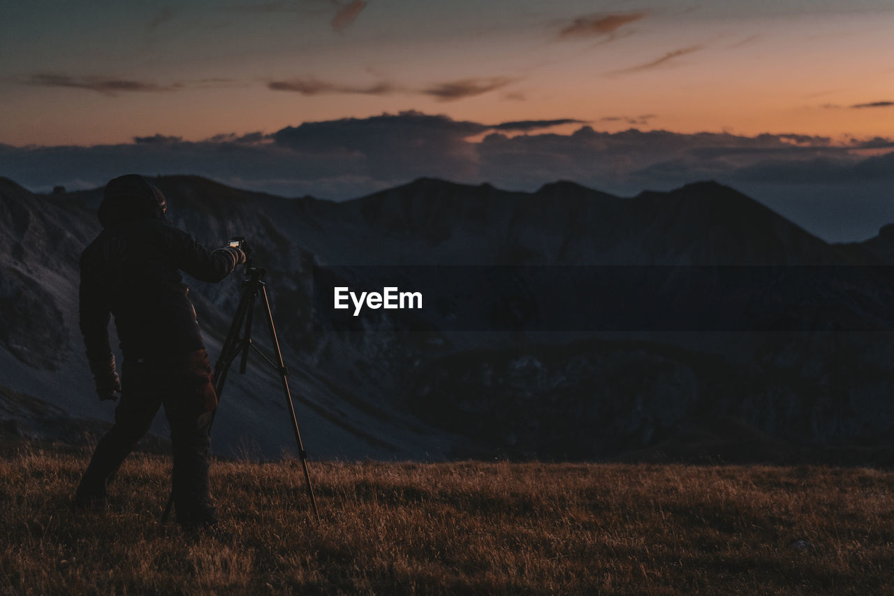 Man photographing on mountain against sky during sunrise