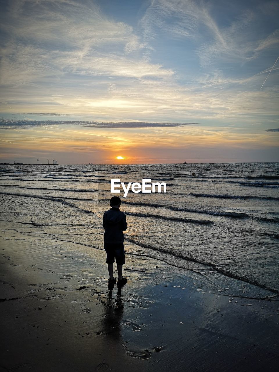 Rear view of boy standing at beach during sunset