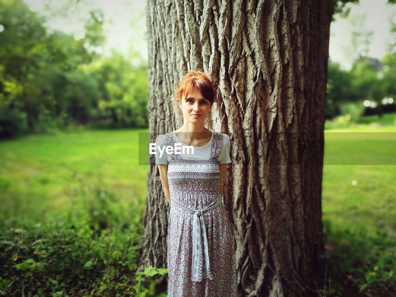 Portrait of young woman standing against tree trunk