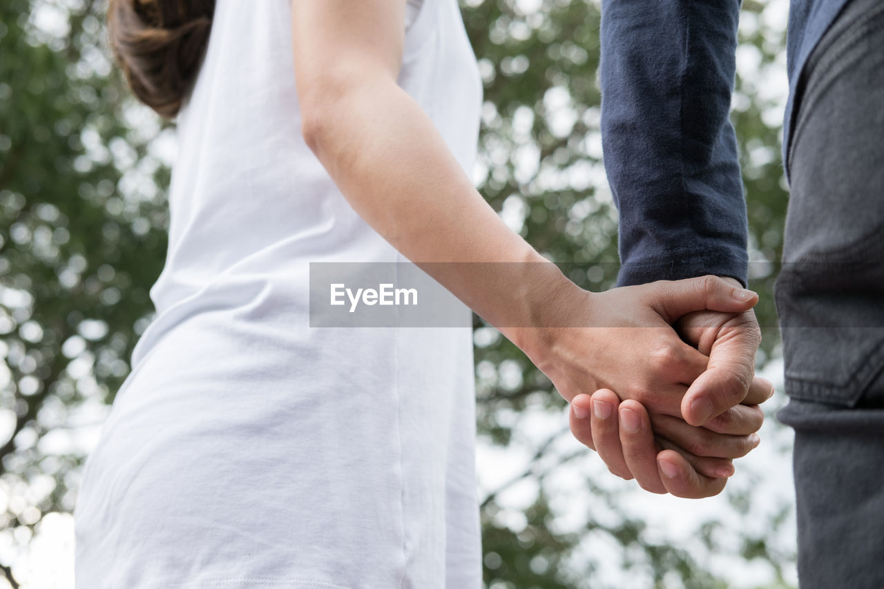 Midsection of couple holding hands while standing at park