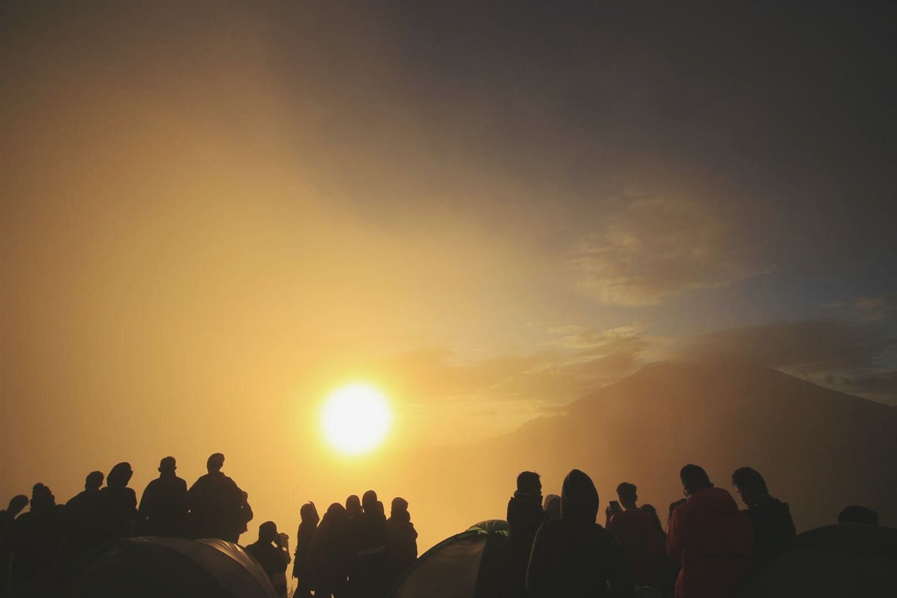 Silhouette people enjoying on mountain against orange sun in sky