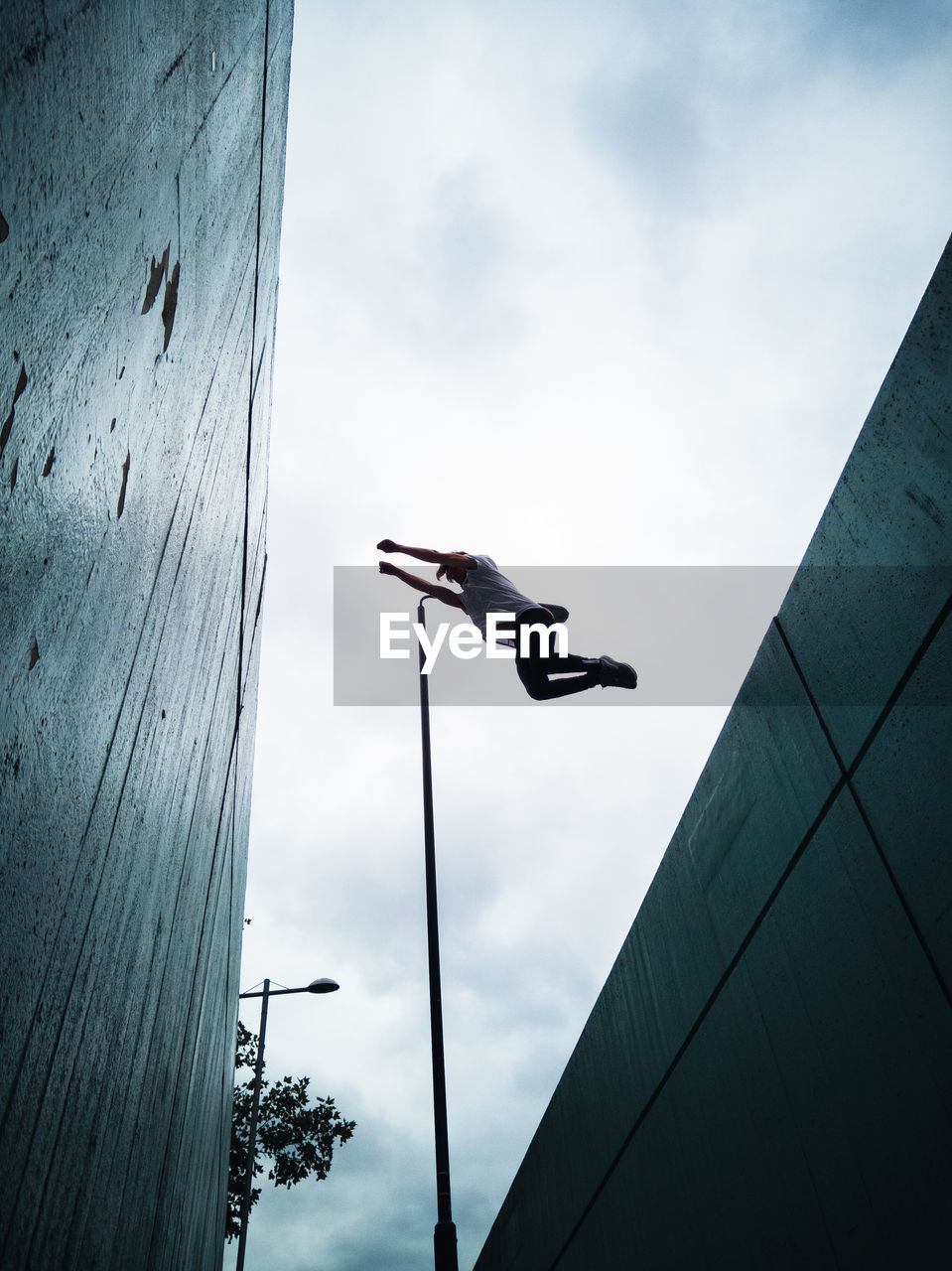 Low angle view of man flying over buildings against cloudy sky