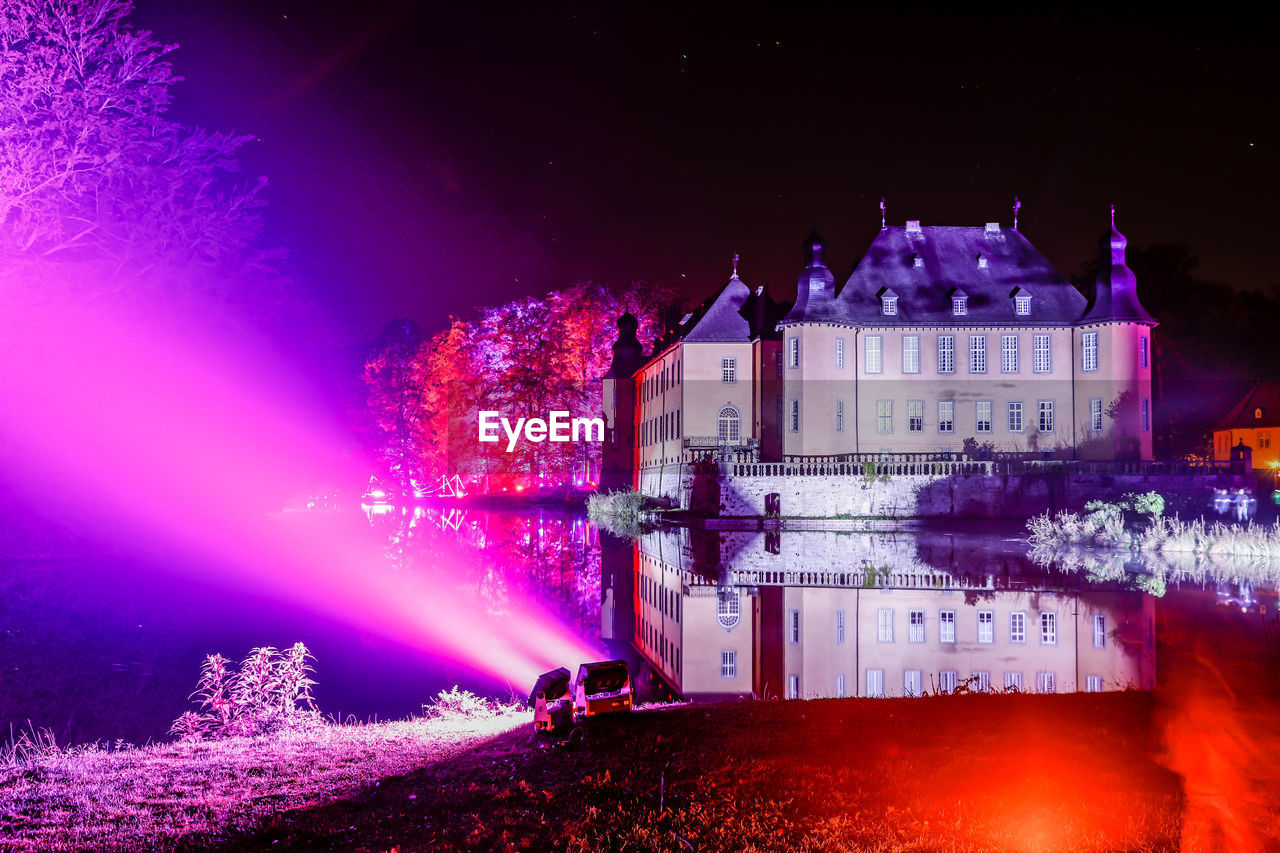 ILLUMINATED BUILDING BY RIVER AGAINST SKY