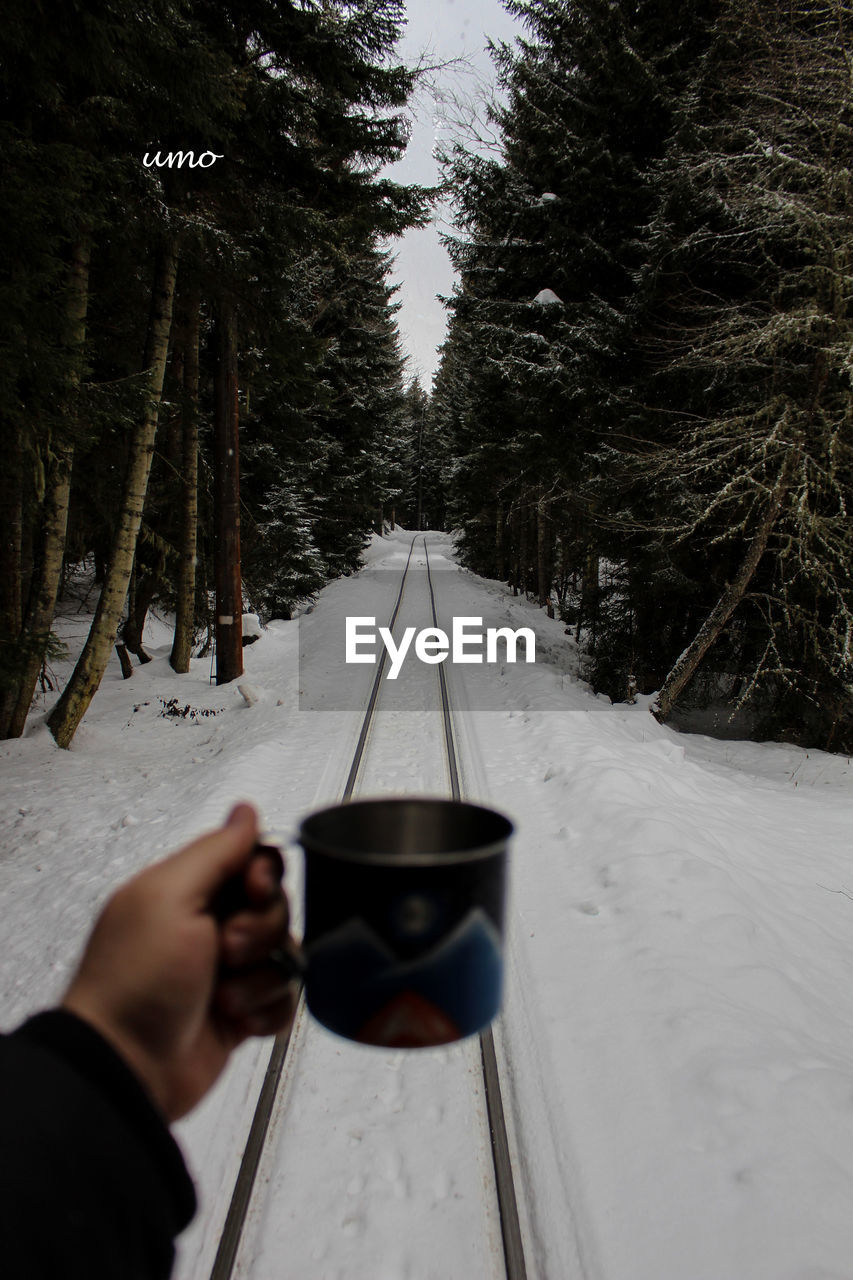 Hand holding cup over railroad tracks during winter