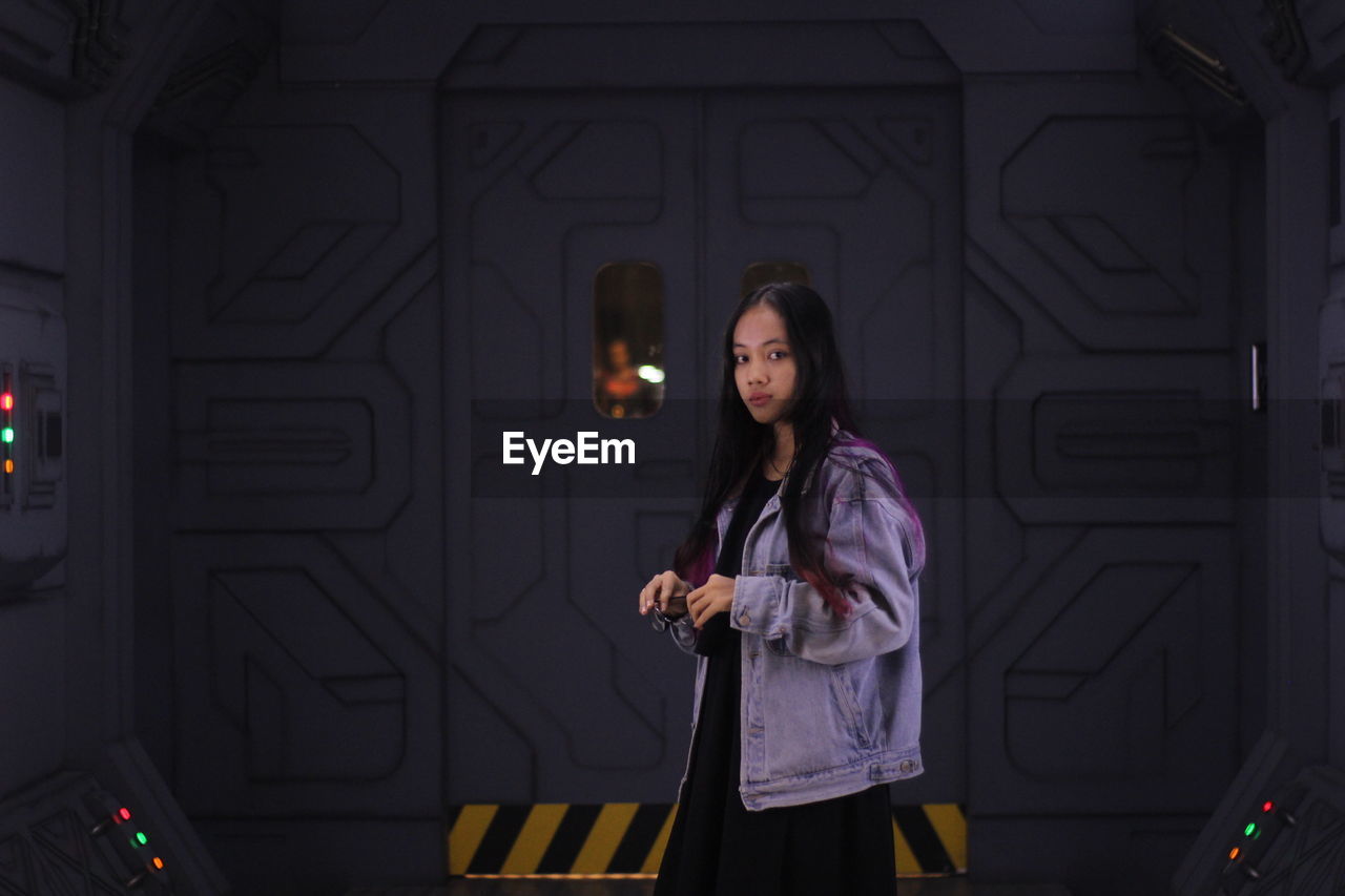 Portrait of young woman standing against door