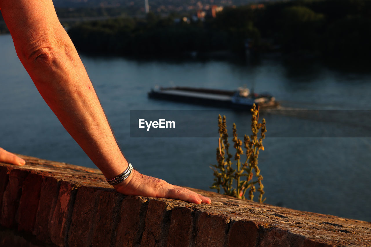 Cropped hands on retaining wall by river