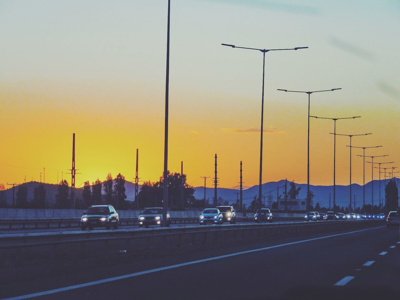 VEHICLES ON ROAD AGAINST SKY DURING SUNSET