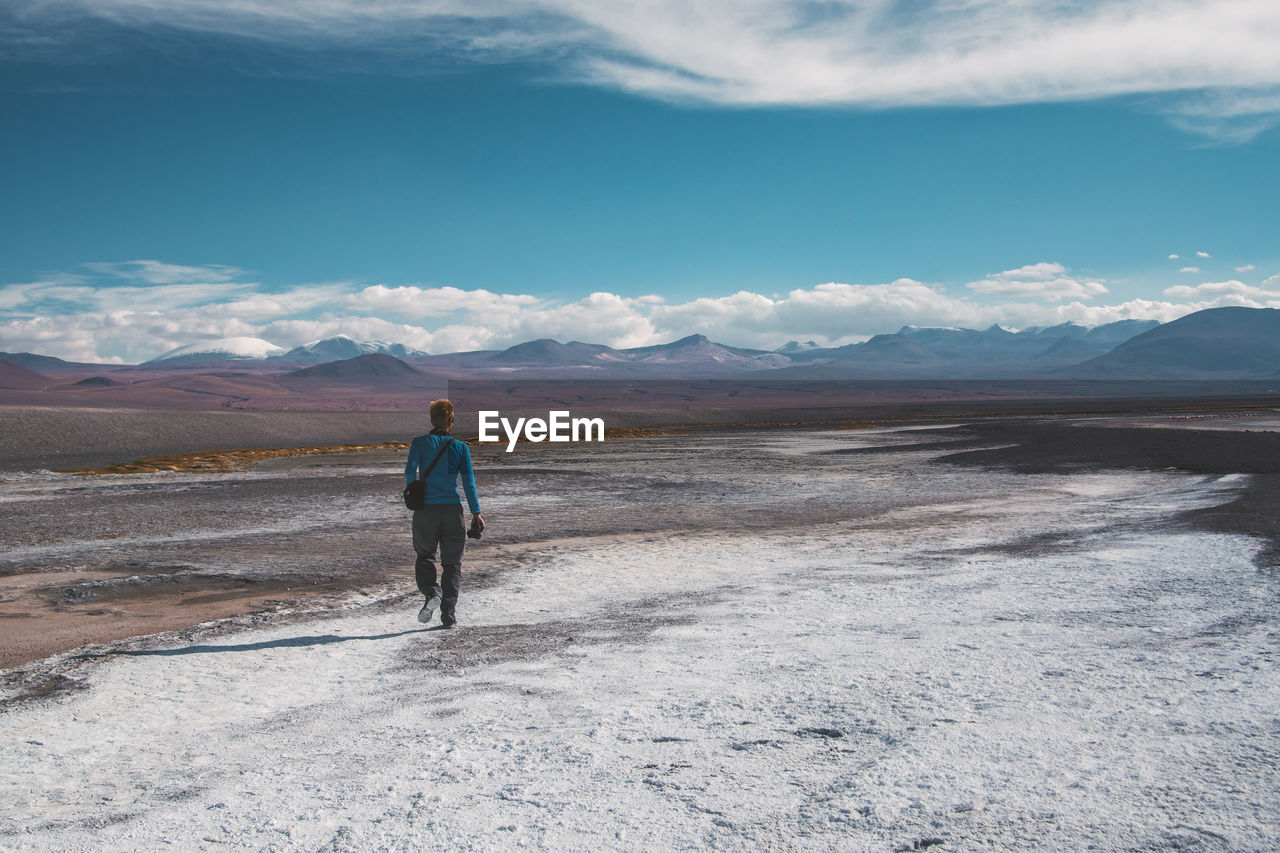 Rear view of man walking on landscape against sky