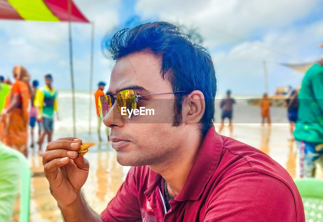 glasses, sunglasses, adult, focus on foreground, men, portrait, headshot, day, group of people, festival, summer, fun, nature, fashion, emotion, outdoors, music festival, event, holding, lifestyles, multi colored, young adult, leisure activity, food and drink, person, crowd, festival goer, happiness, sky, looking