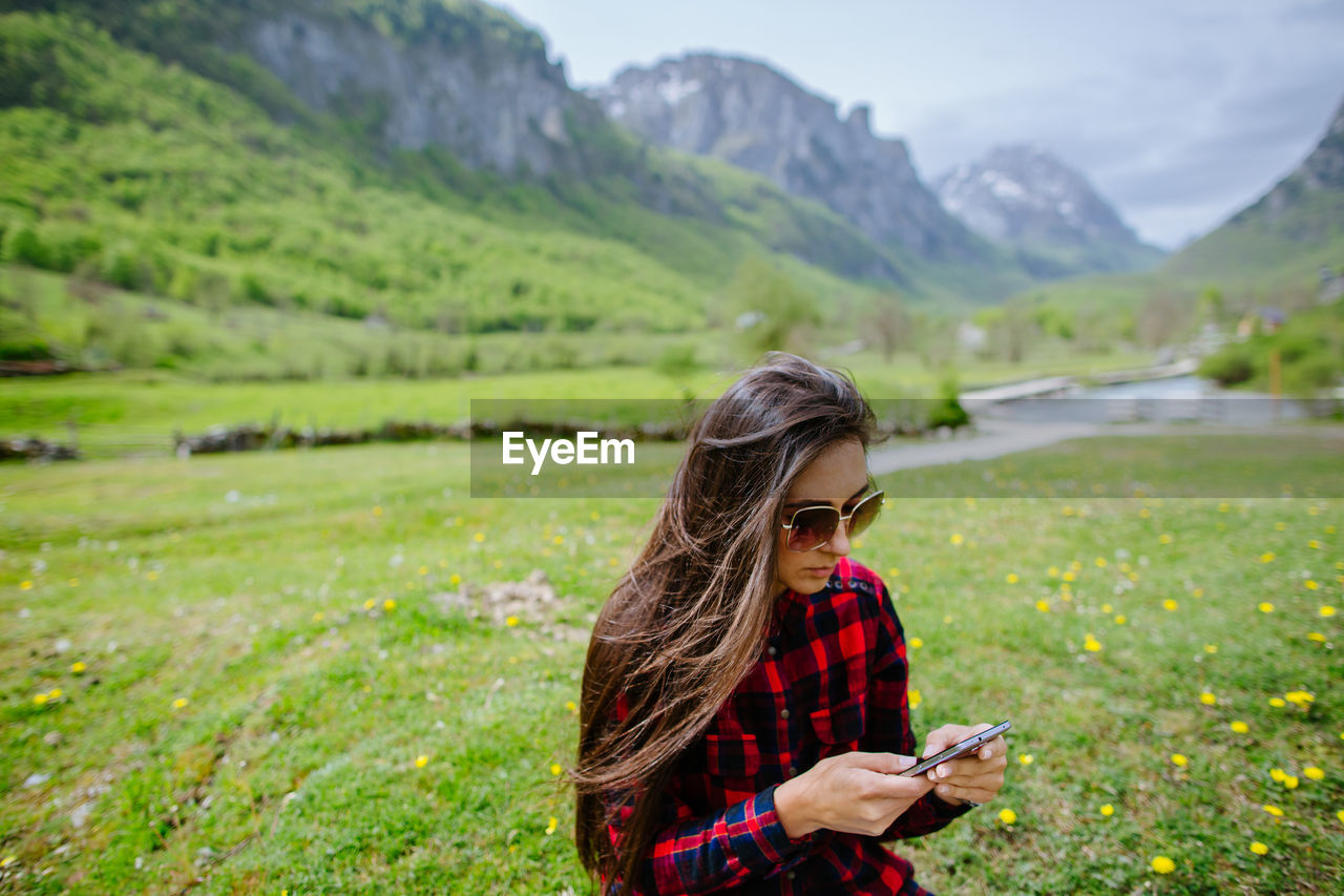 Woman holding smart phone while standing on field