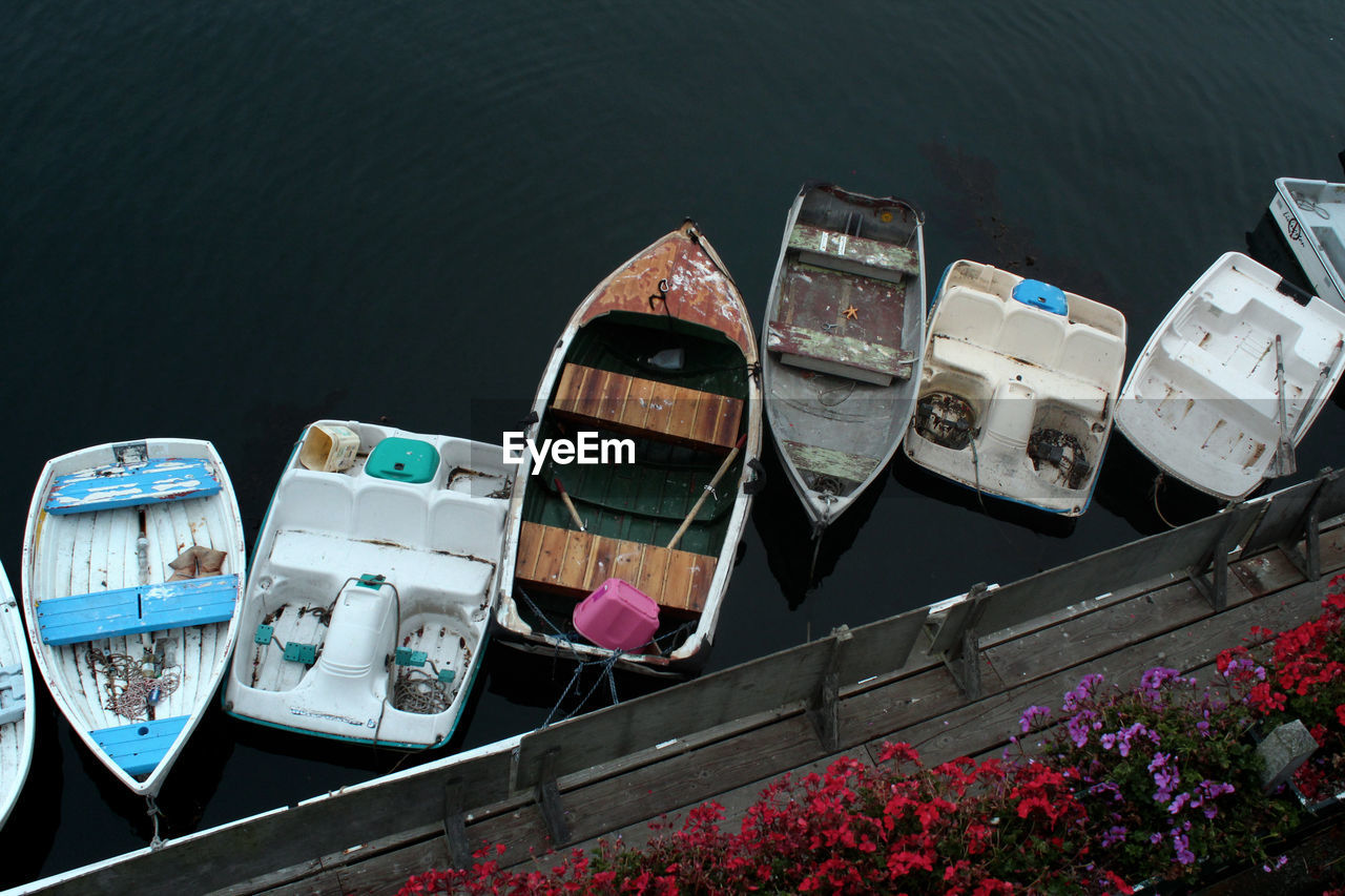 High angle view of boats moored in water, wooden board dock with flowers.