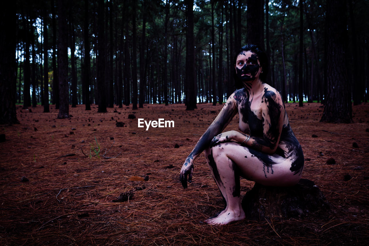 Naked woman covered with paint while sitting in forest