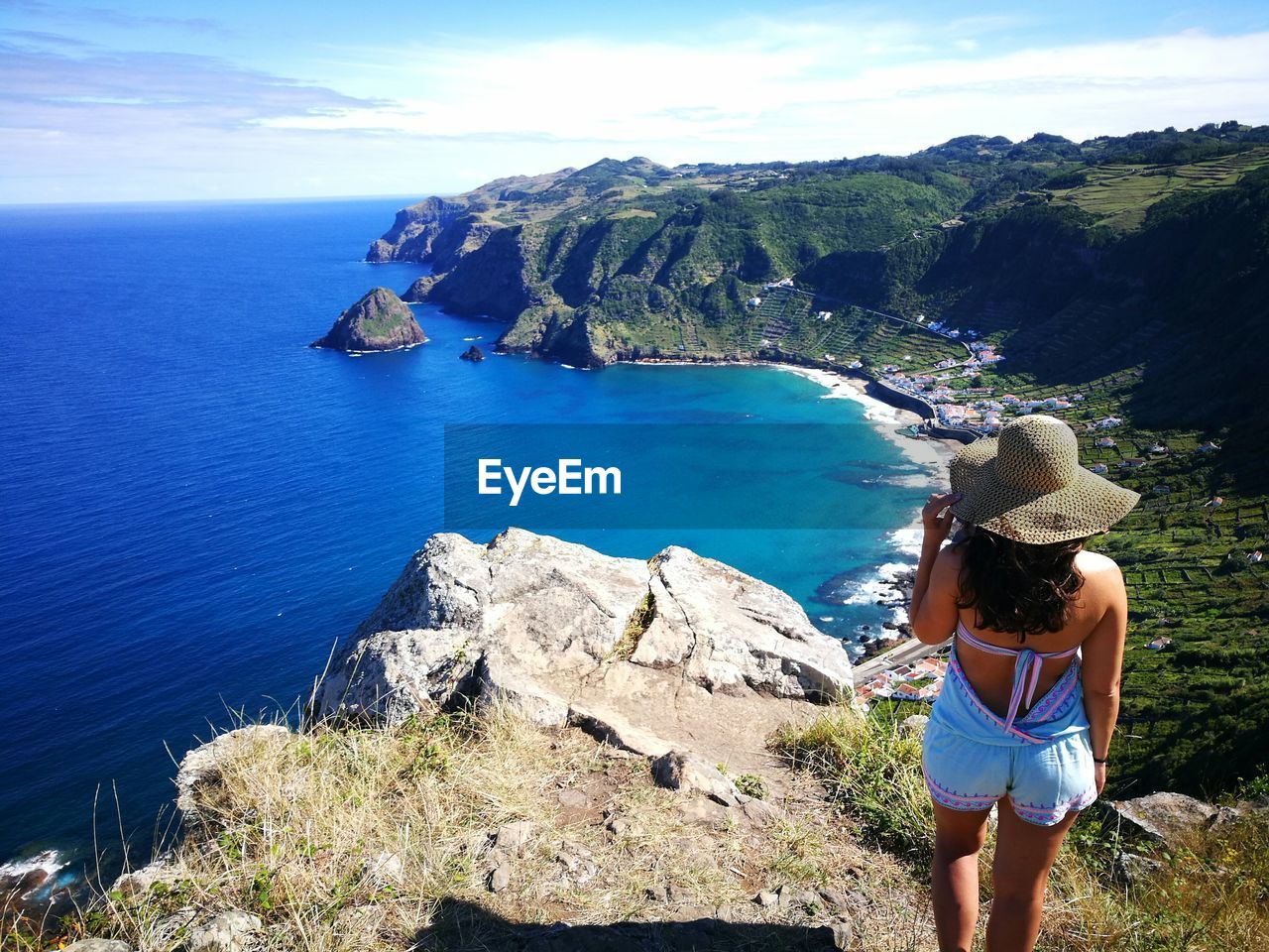 Rear view of woman standing on cliff by sea