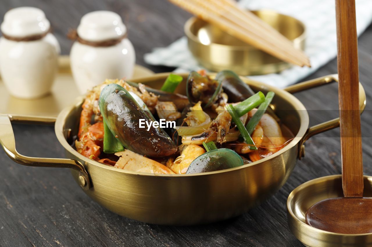 Mix seafood soup on golden pan, on wooden table. close up