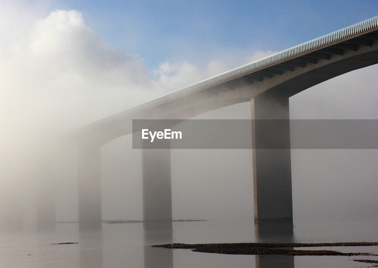 Bridge over river against sky during foggy weather