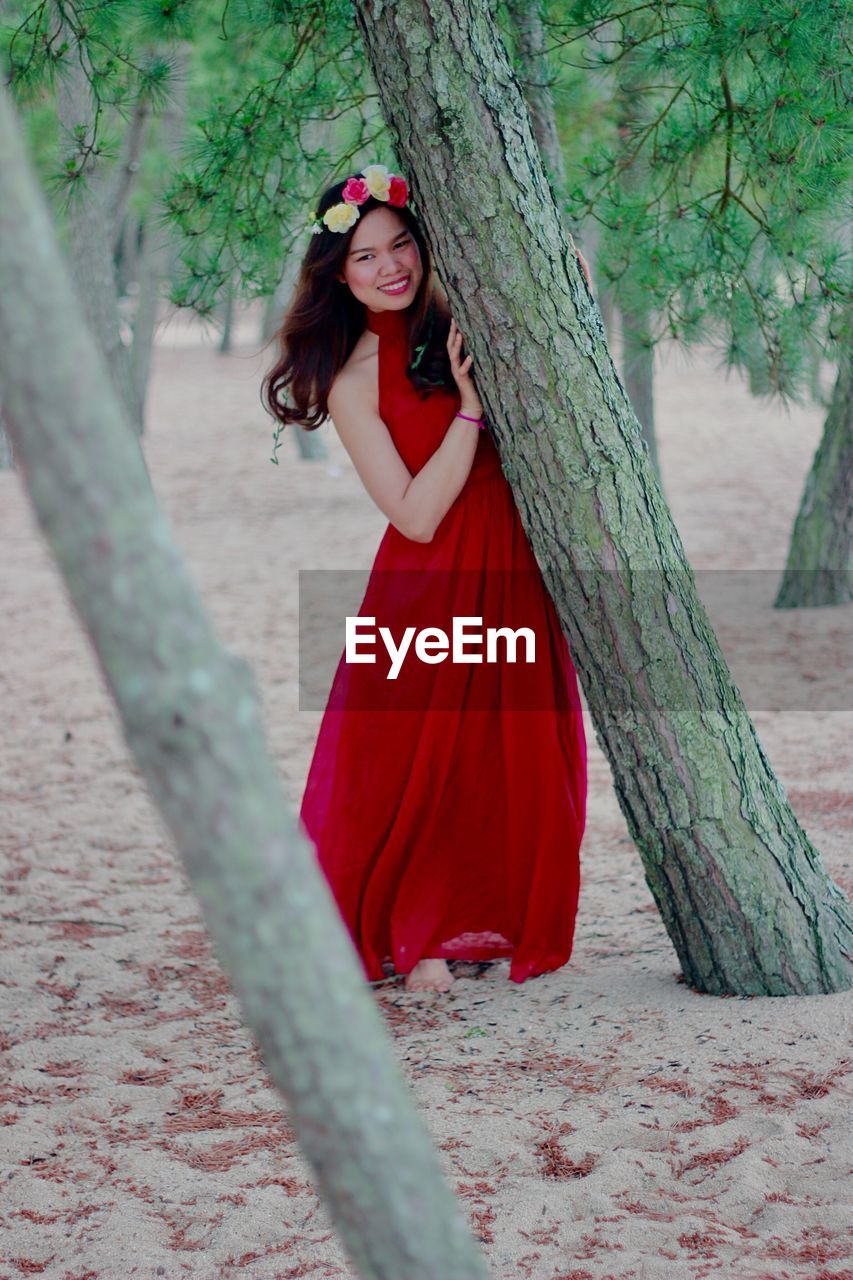 Portrait of smiling woman standing by tree trunk