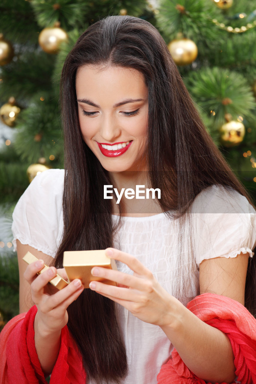 Young woman opening christmas present against christmas tree