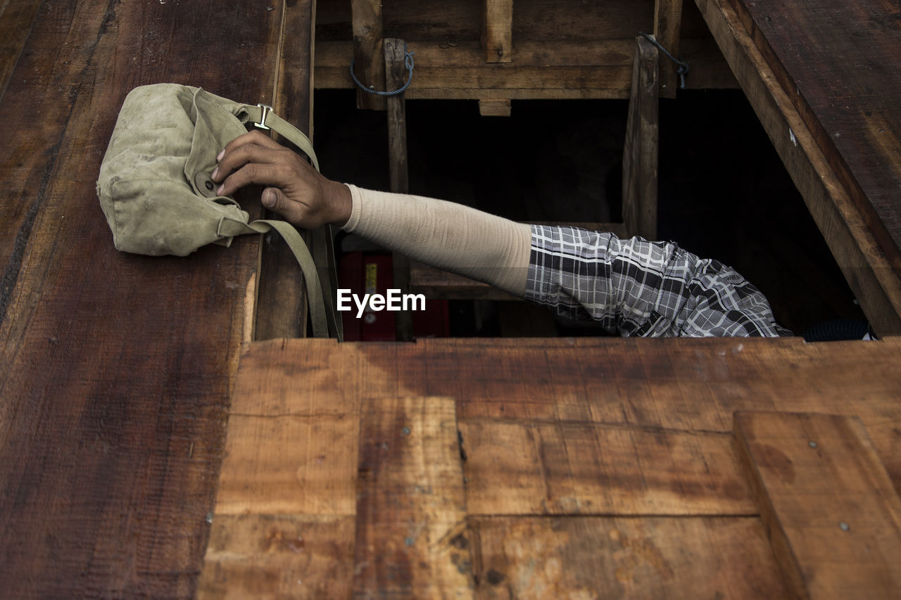 Cropped image of man by shoulder bag on wooden floor