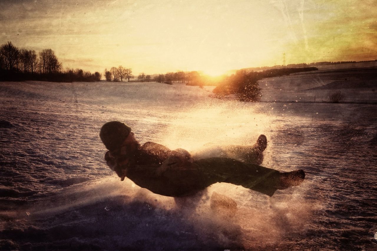 Full length of man riding sled on field against sky at sunset during winter