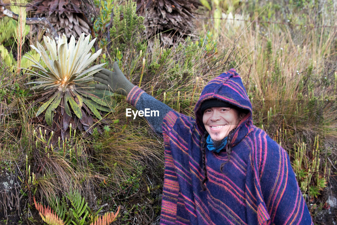 Colombian native american man in traditional clothing pointing on plant