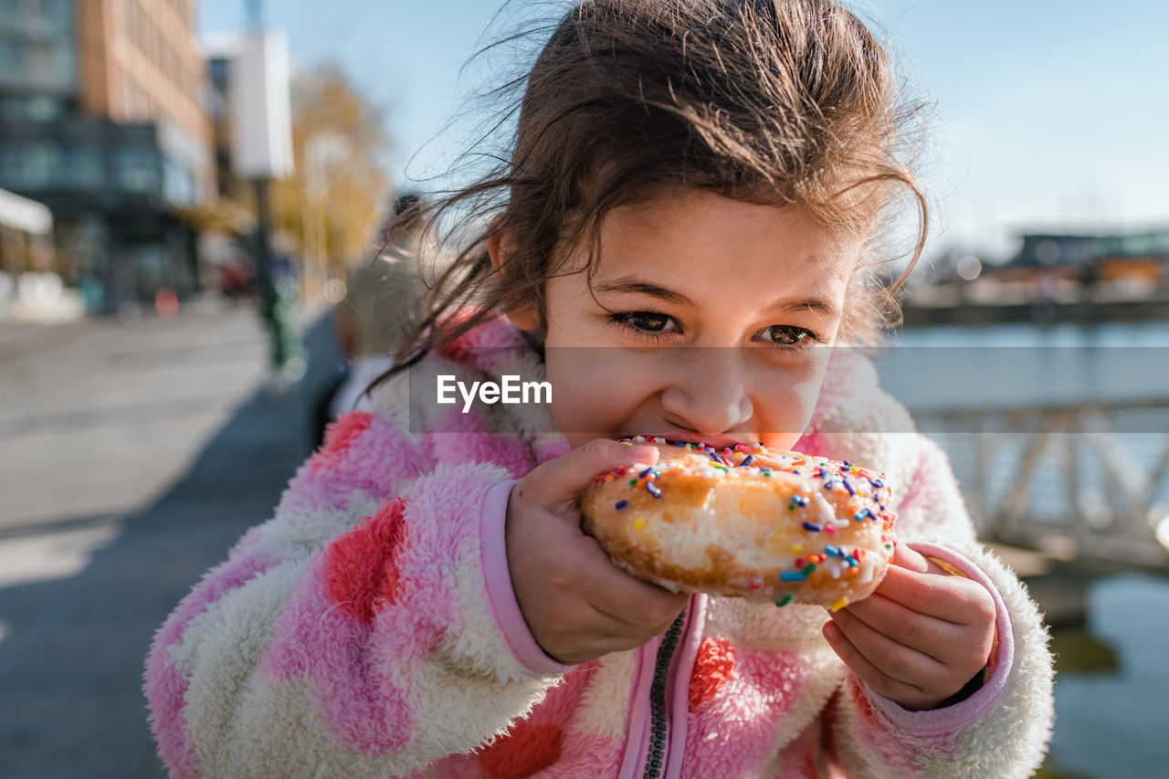 Young girl eating donut with sprinkles outside
