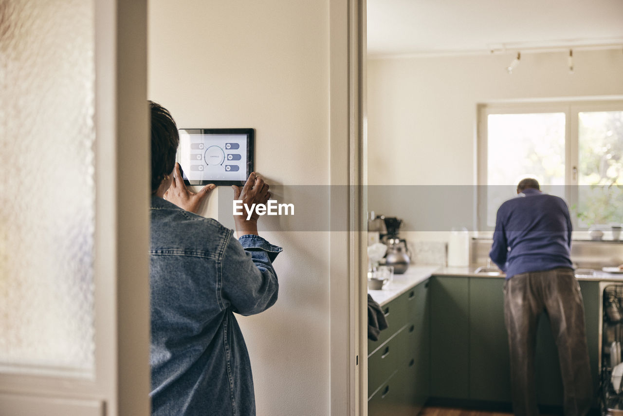 Rear view of woman using digital tablet mounted on wall at home