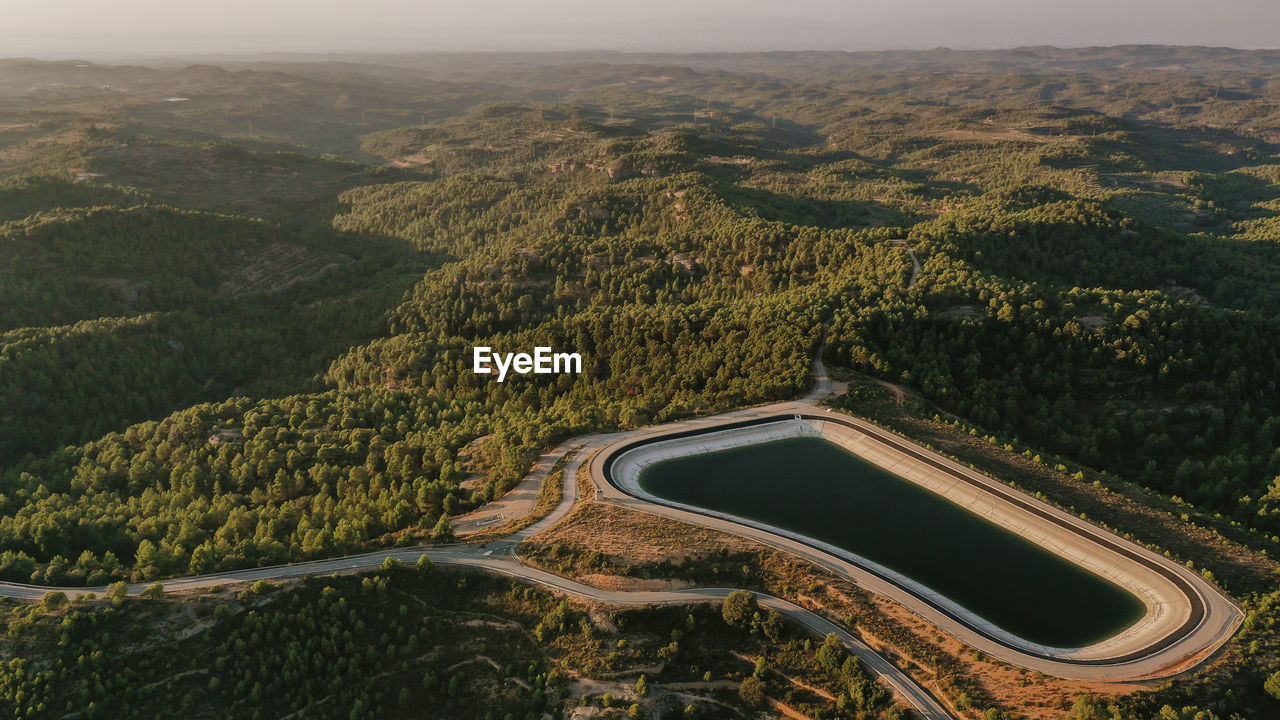 Aerial view of mountaintop reservoir at dusk with forested hills in background