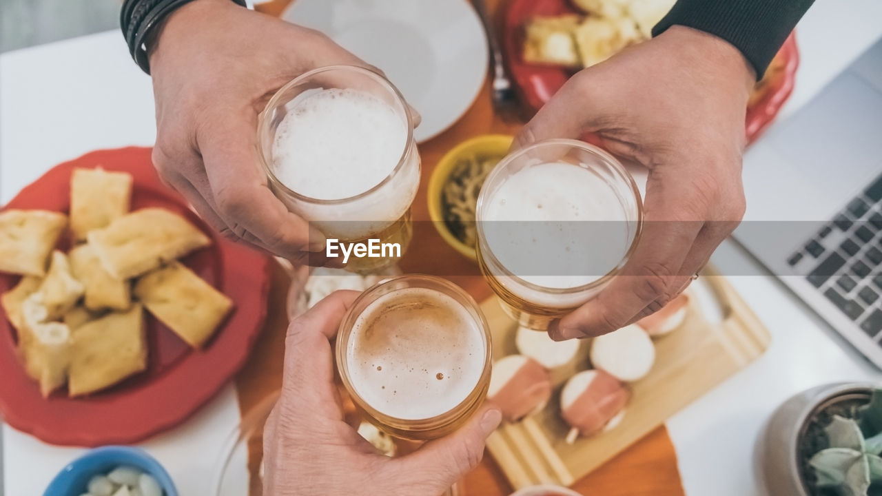 Toast with friend enjoying dinner together.  table with foods and glasses of beer in hands cheer up