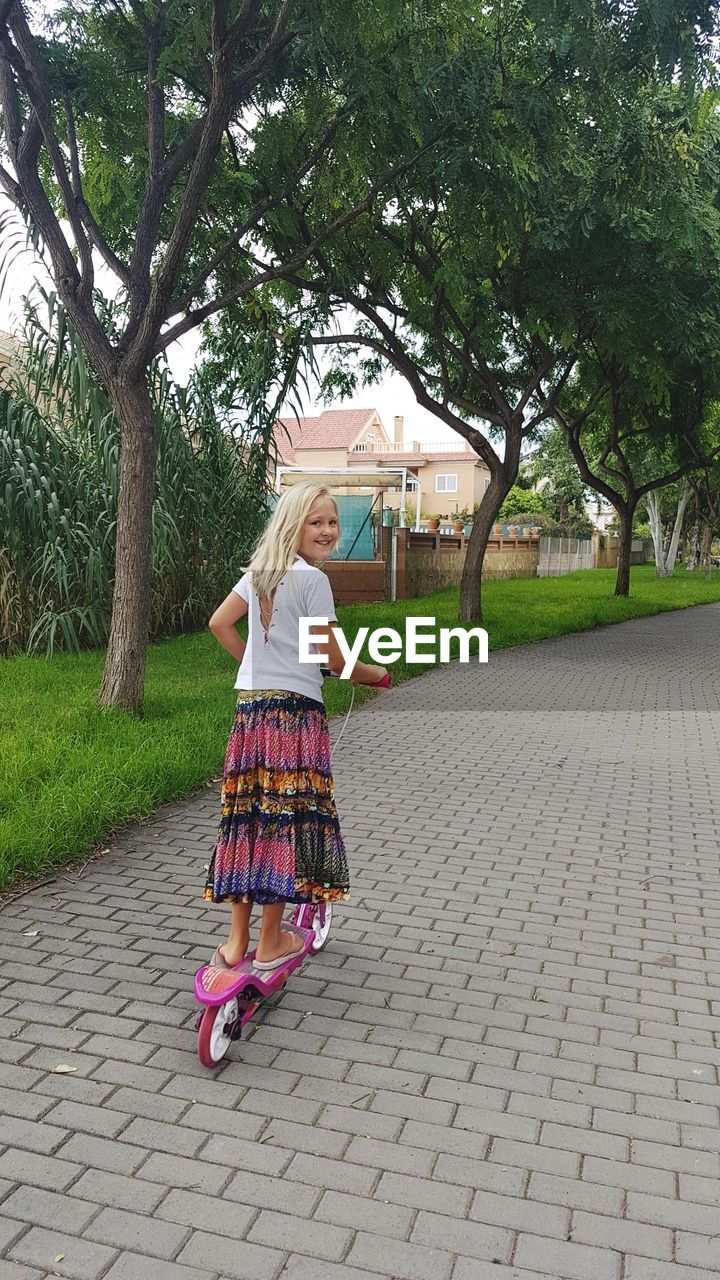 GIRL STANDING ON FOOTPATH BY TREE