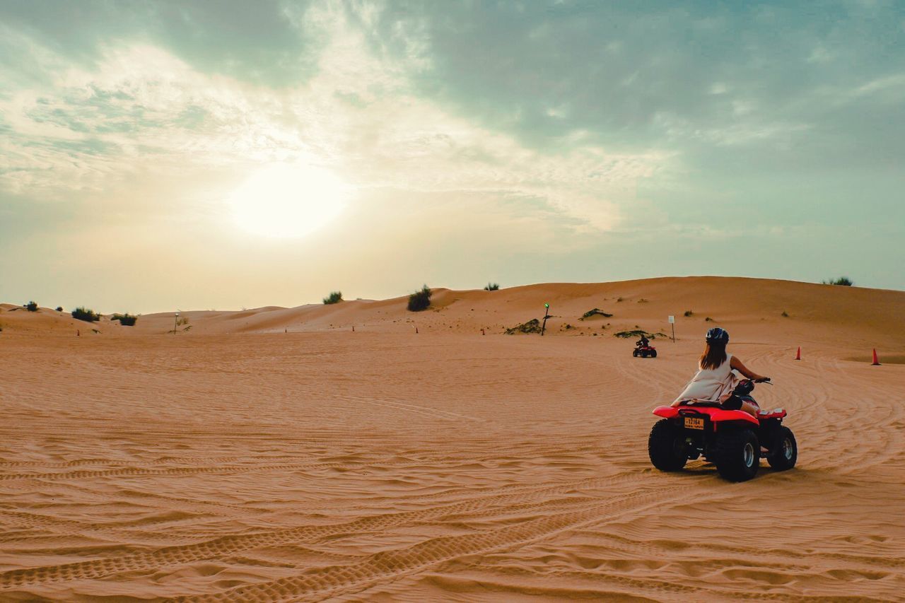 MAN RIDING MOTORCYCLE IN DESERT AGAINST SKY