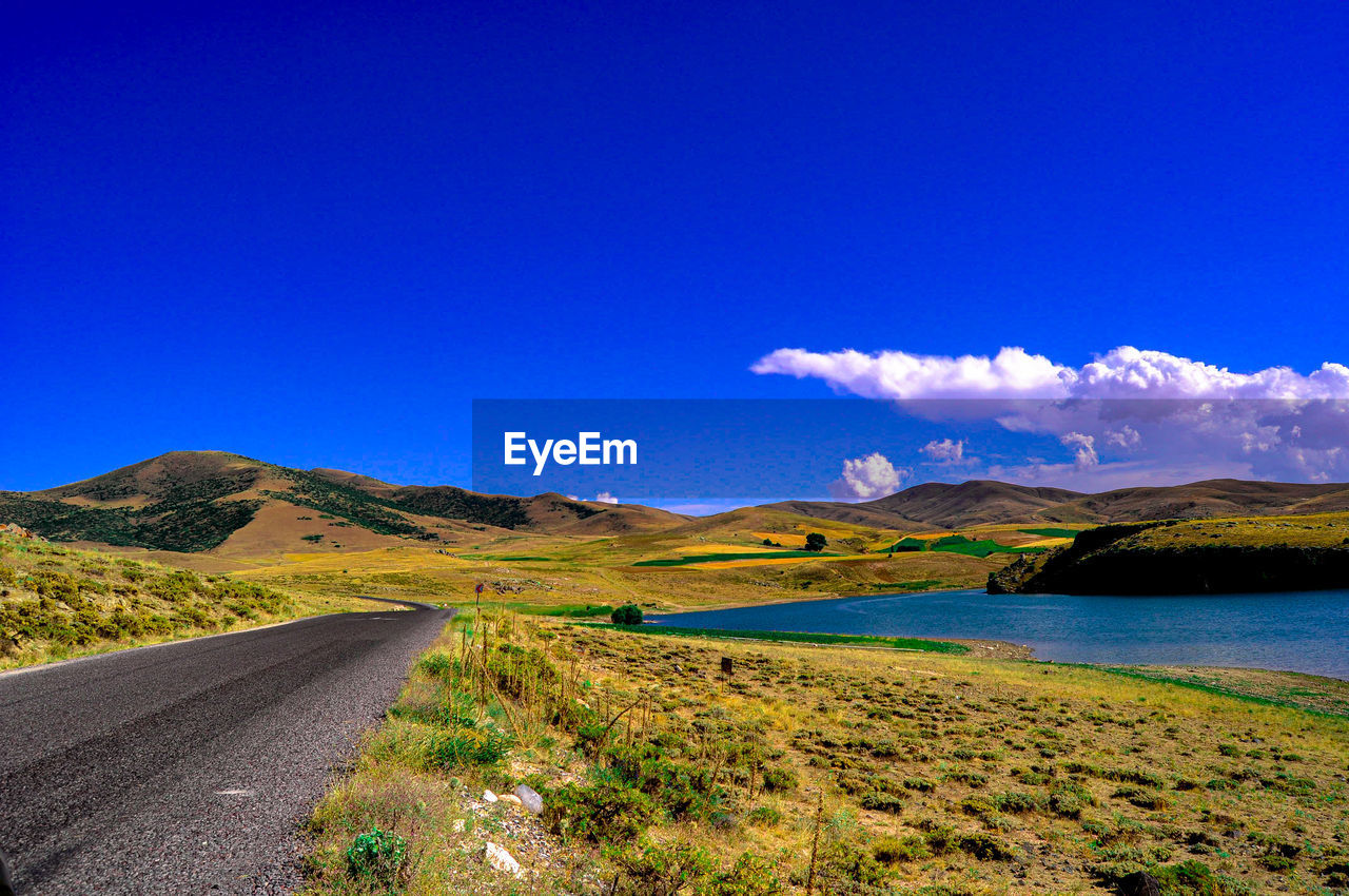 Scenic view of road by mountains against blue sky