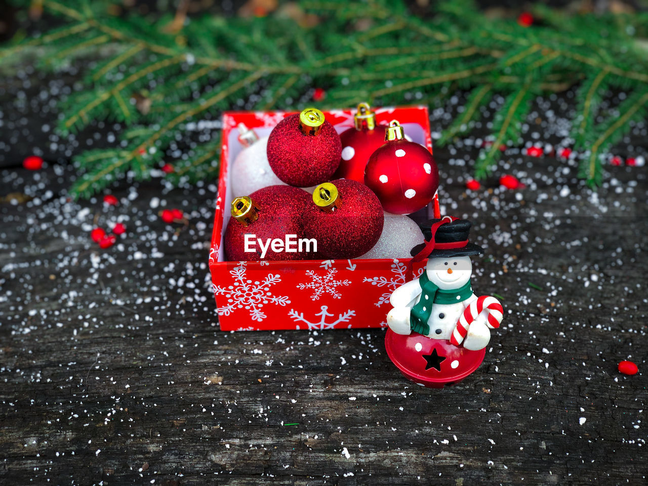 Red and white christmas baubles and a tiny snowman placed on a rustic table decorated with fake snow