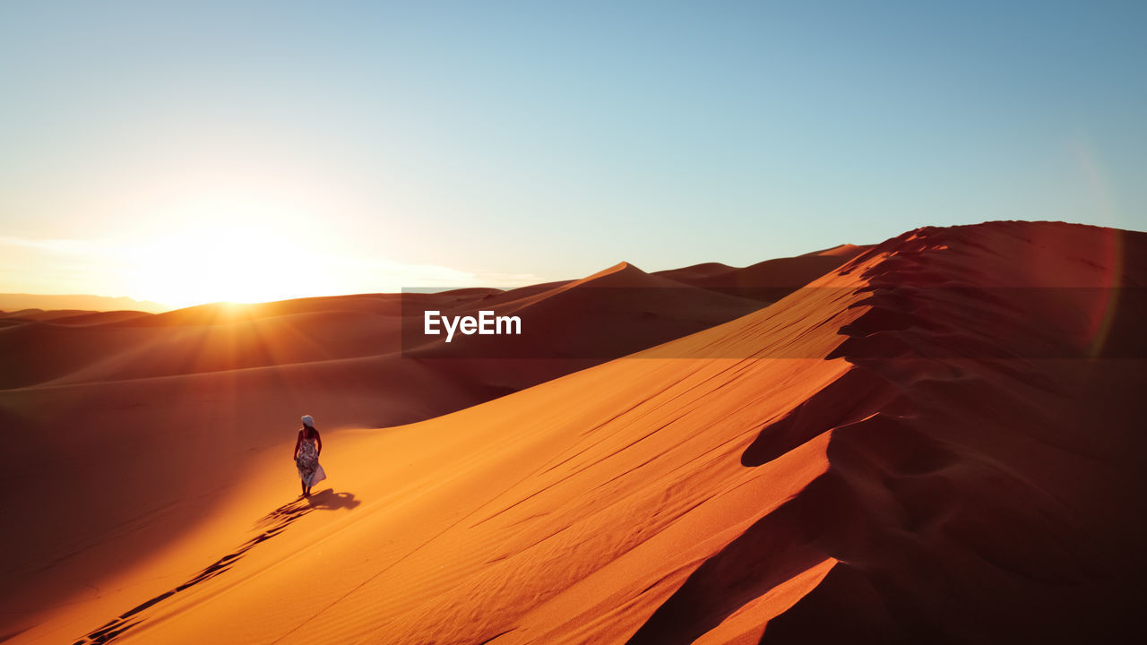 Silhouette of woman on sand dune in desert against clear sky