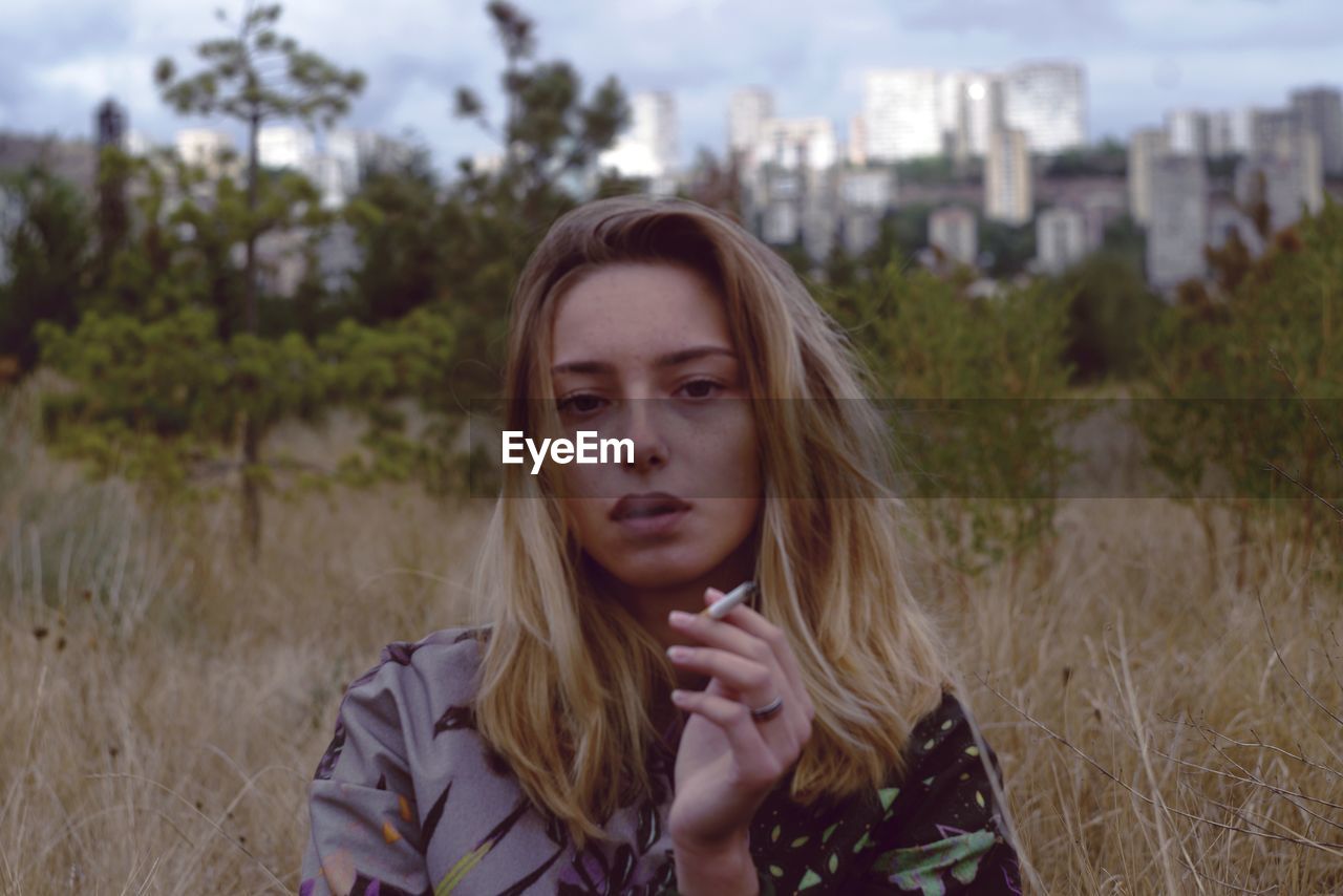 Portrait of young woman smoking on field