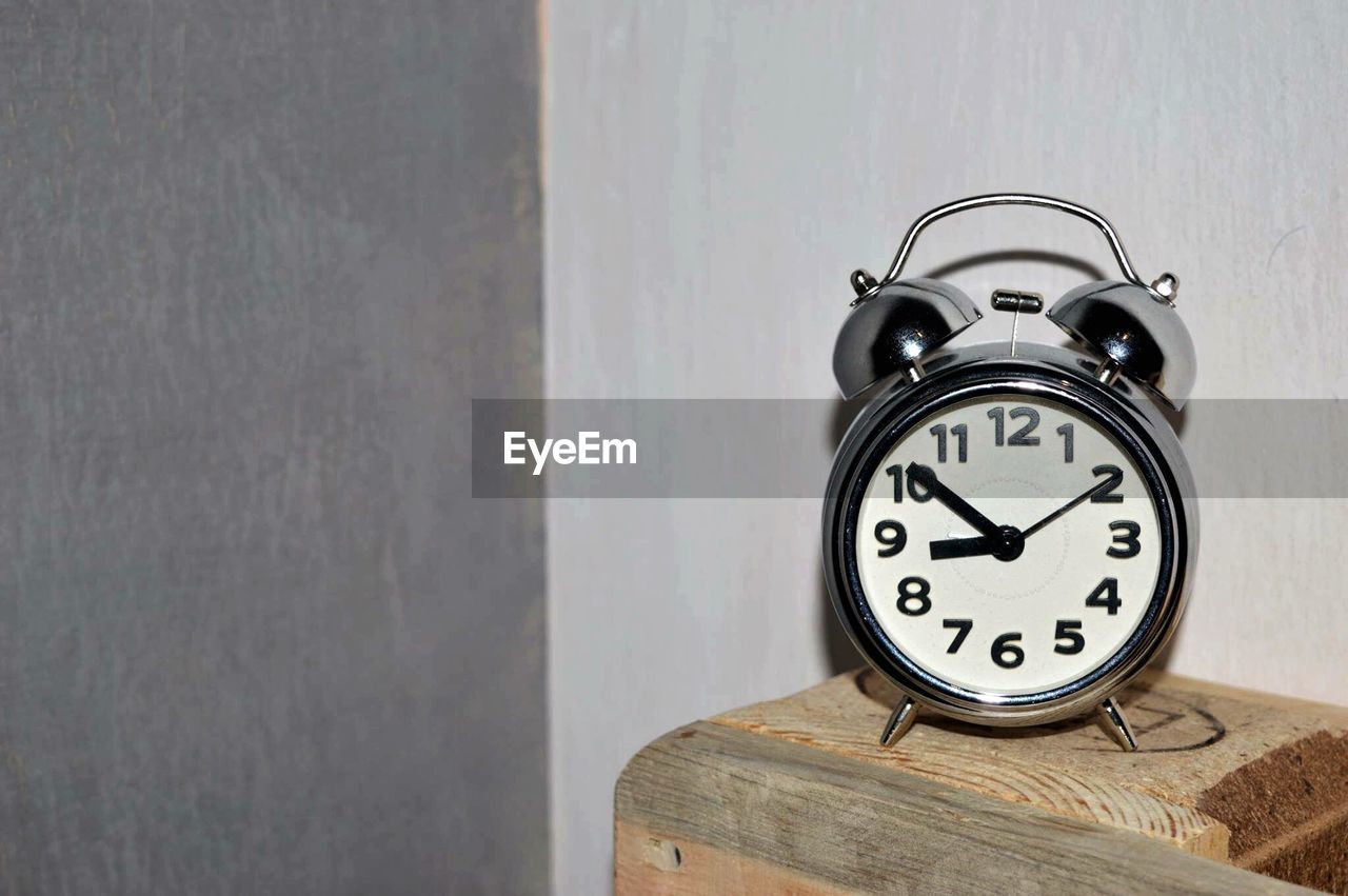 Close-up of alarm clock on wooden table against wall