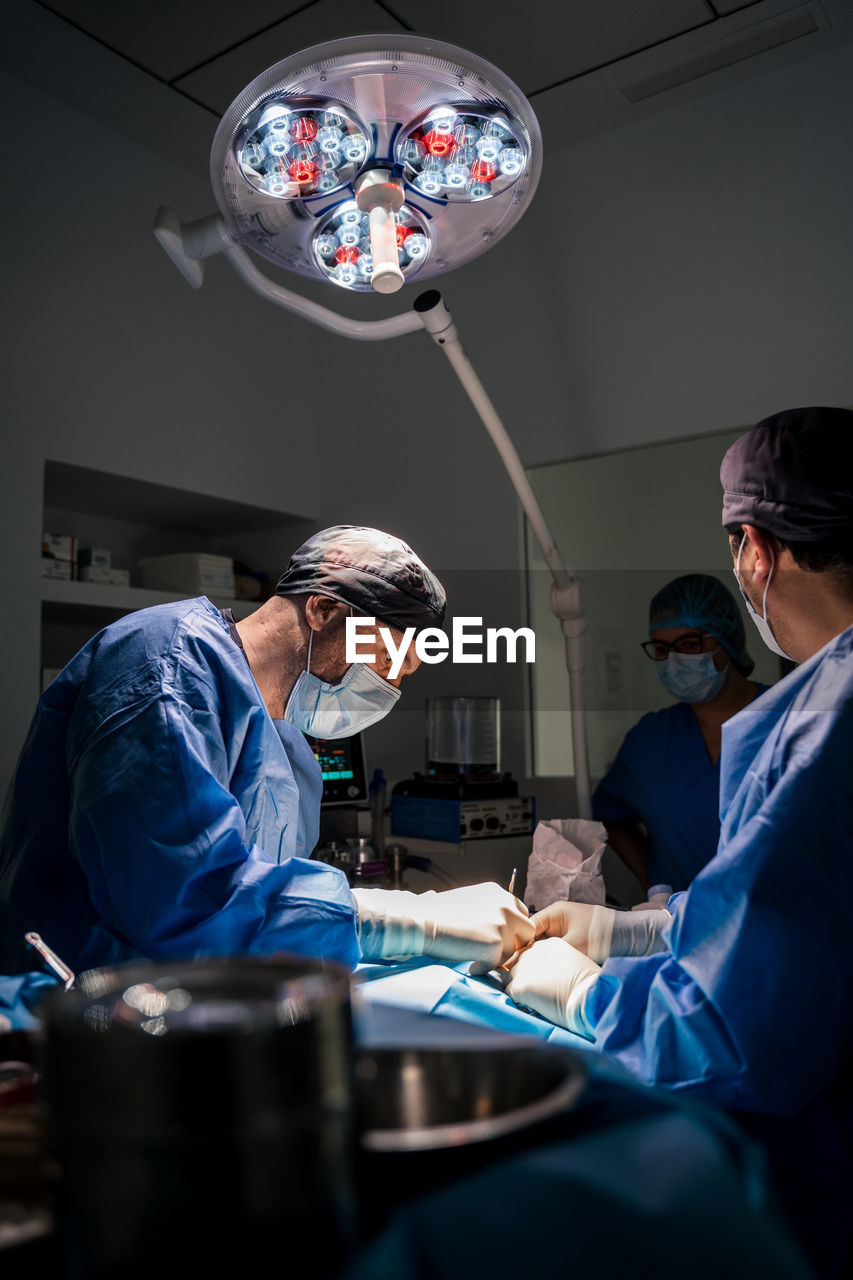 Veterinarian surgeons and nurses in uniform concentrating and operating dog using special equipment in operating room of contemporary hospital