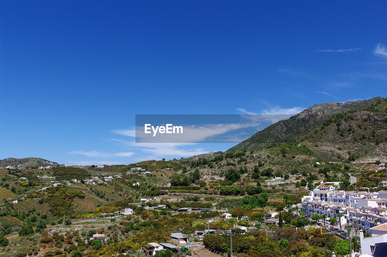 Scenic view of town by mountains against blue sky