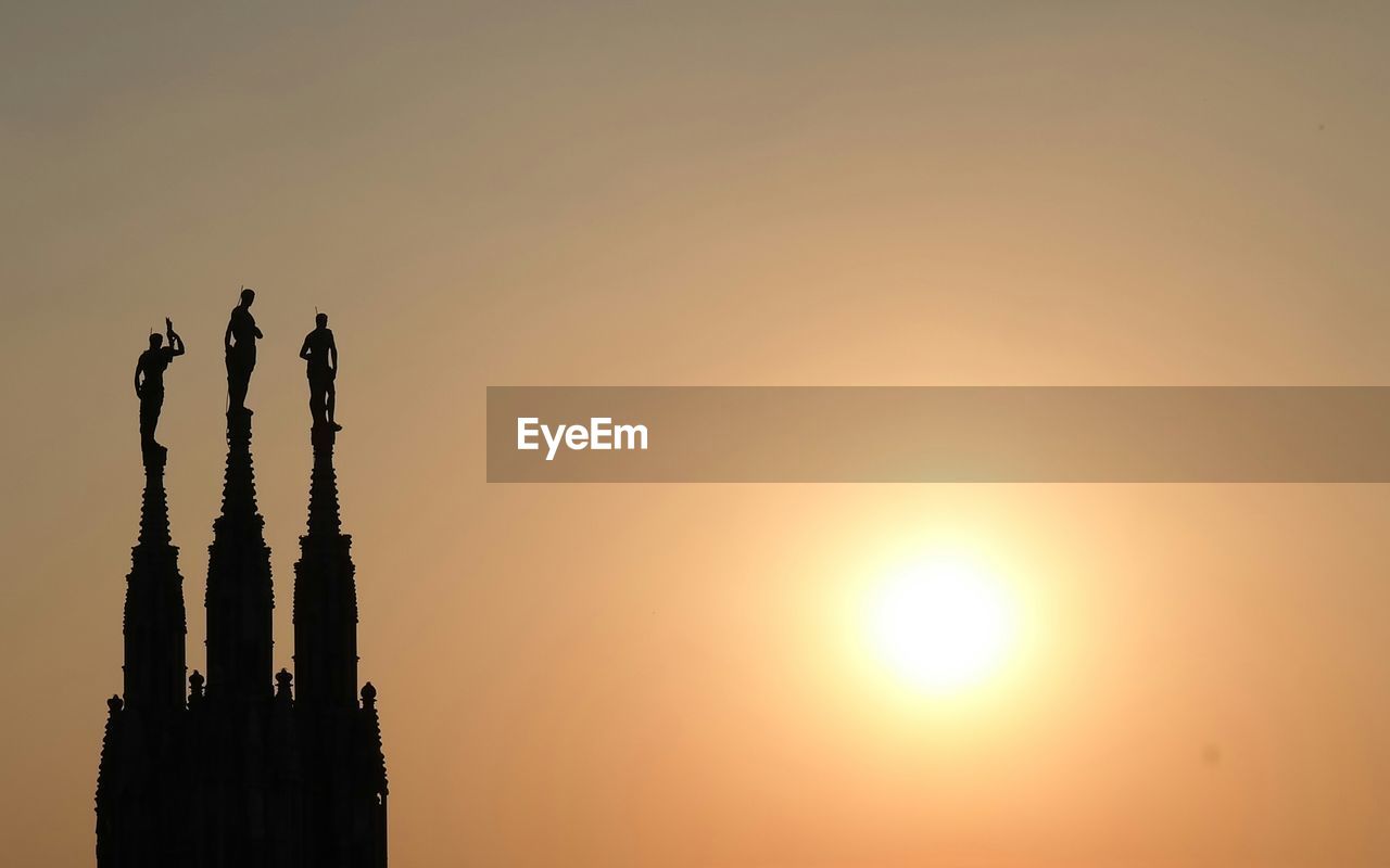 Silhouette spire of milan cathedral against orange sky during sunset