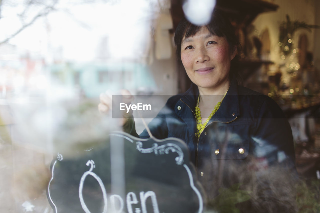 Female owner hanging open sign on window of garden center seen through glass