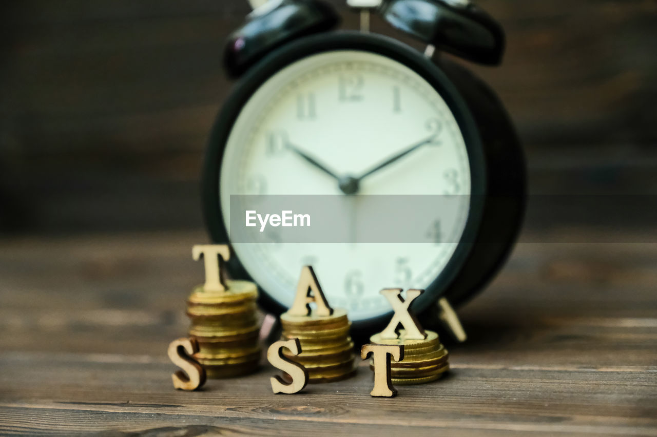 Close-up of coins with tax text and alarm clock on table