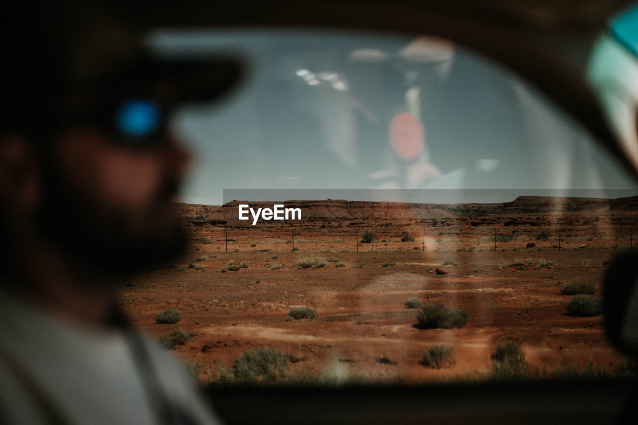 Man driving car against landscape seen through window