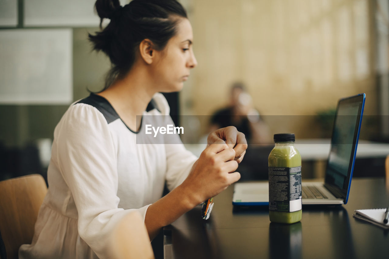 Businesswoman eating food and having healthy drink while using laptop at office desk