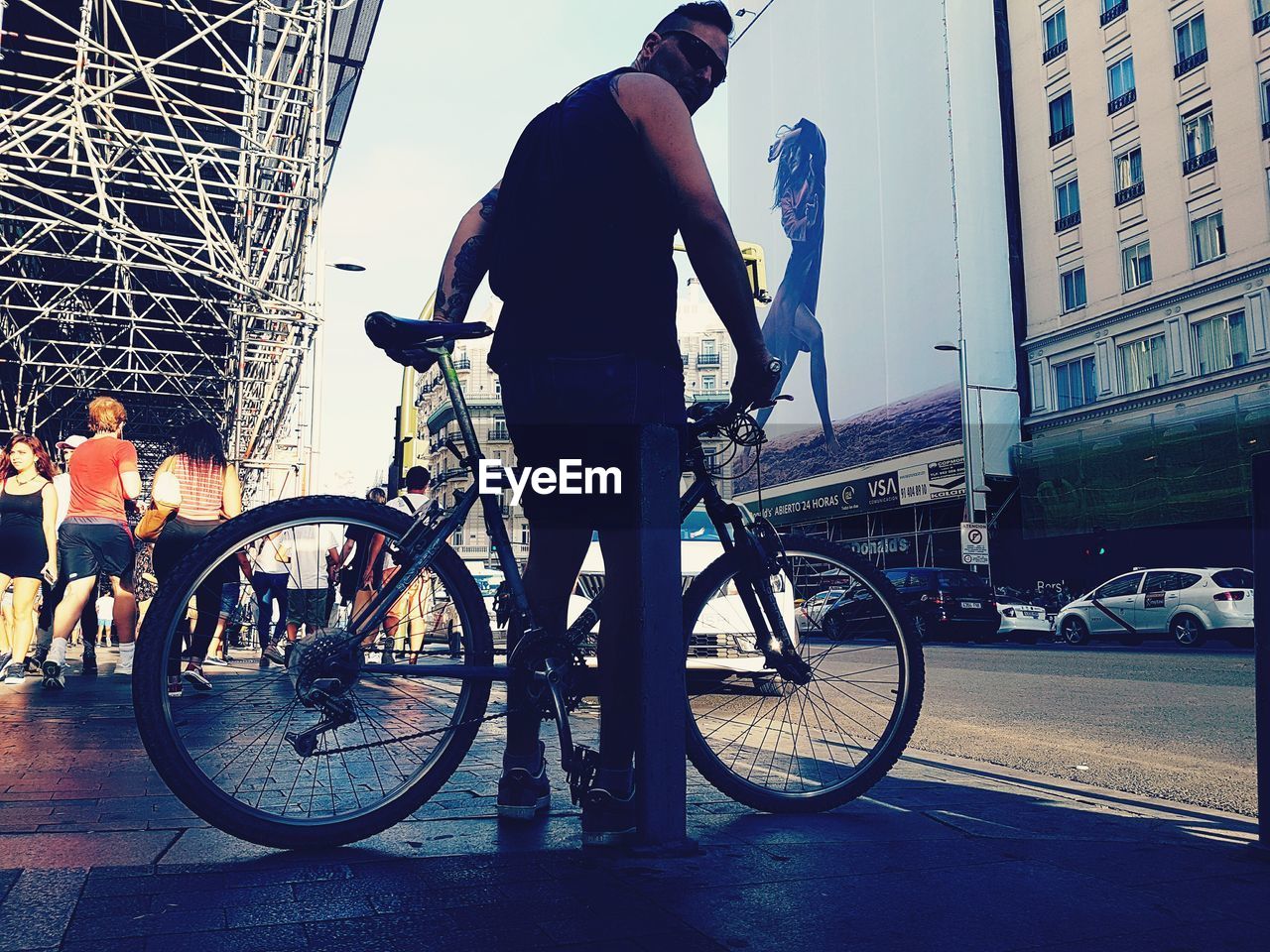 MAN WITH BICYCLE ON ROAD IN CITY