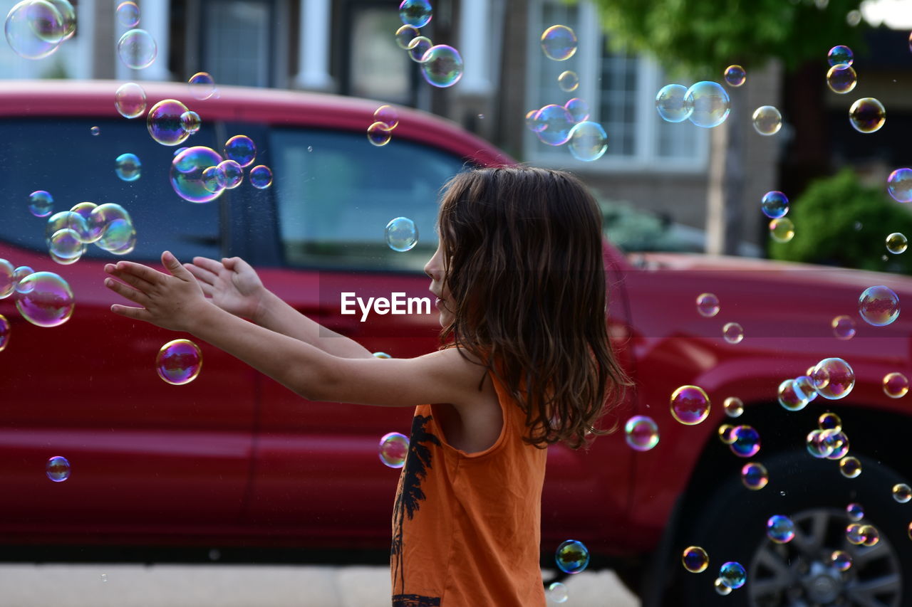 Side view of cute girl playing with bubbles at street