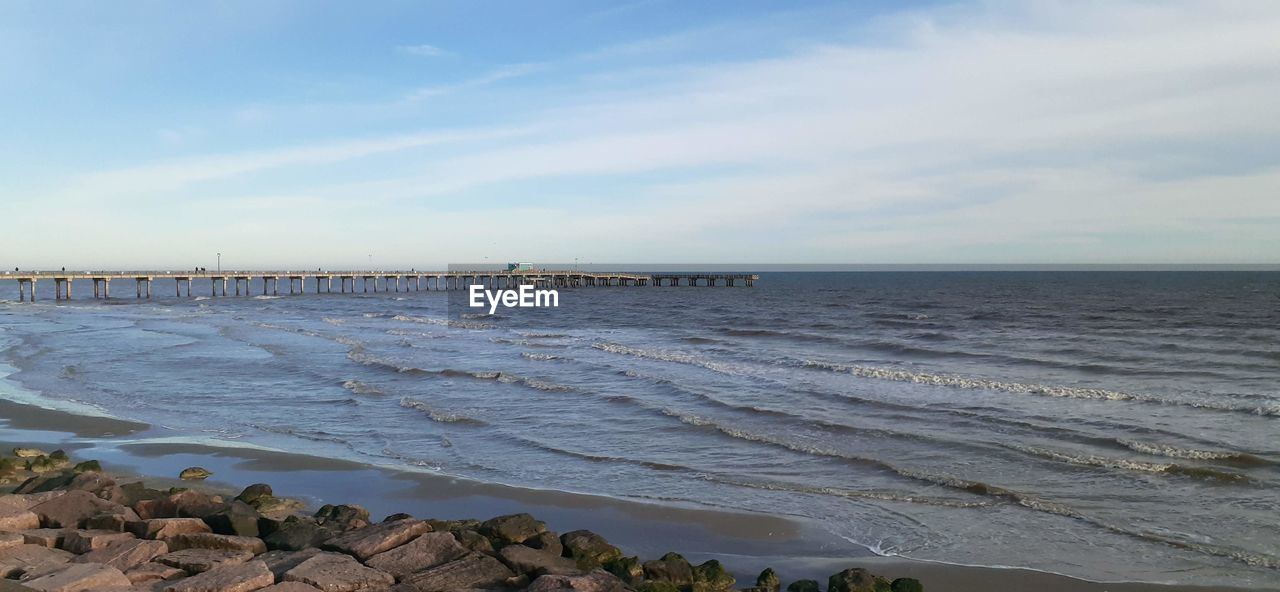 WOODEN POSTS ON BEACH AGAINST SKY